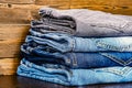 The concept of casual style in clothing. A stack of jeans in different shades of color on a wooden table.