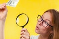 The concept of checking counterfeit money. A blond woman with interest in looking at a dollar bill through a magnifying glass, Royalty Free Stock Photo