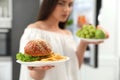 Concept of choice. Woman holding fruits and burger with French fries in kitchen, closeup Royalty Free Stock Photo