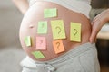 Concept of choosing baby name. cropped shot of pregnant woman with question marks on paper stickers on tummy Royalty Free Stock Photo