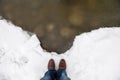 Concept of cold winter man legs in jeans and feet in boots shoes standing on clean white snow before frozen water of lake with Royalty Free Stock Photo