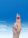 Human or female hands with two fingers painted with a red heart and smiley faces over cloud blue sky Royalty Free Stock Photo