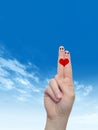 Human or female hands with two fingers painted with a red heart and smiley faces over cloud blue sky Royalty Free Stock Photo