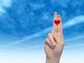 Human or female hands with two fingers painted with a red heart and smiley faces over cloud blue sky Royalty Free Stock Photo