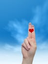 Human or female hands with two fingers painted with a red heart and smiley faces over cloud blue sky Royalty Free Stock Photo