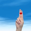 Human or female hands with two fingers painted with a red heart and smiley faces over cloud blue sky Royalty Free Stock Photo