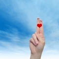 Human or female hands with two fingers painted with a red heart and smiley faces over cloud blue sky Royalty Free Stock Photo