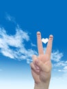 Human or female hands with two fingers painted with a white heart and smiley faces over cloud blue sky Royalty Free Stock Photo