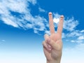 Human or female hands with two fingers painted with a white heart and smiley faces over cloud blue sky Royalty Free Stock Photo