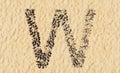 Stones on beach sand handmade symbol shape, golden sandy background, sign of W