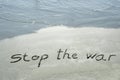 Stop de war handwritten text in sand on a beach with waves in an exotic island for no war, freedom