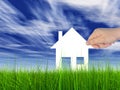 White paper house held in hand by a man in a green summer grass over a blue sky background with clouds Royalty Free Stock Photo
