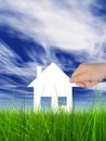 White paper house held in hand by a man in a green summer grass over a blue sky background with clouds Royalty Free Stock Photo