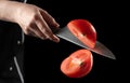 The concept of cooking and profession.. chef cuts a tomato a knife on the fly on a black background. Royalty Free Stock Photo