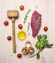 Concept cooking raw beef steak, rosemary, wooden hammer for beating the meat, oil, herbs and spices wooden rustic background to Royalty Free Stock Photo