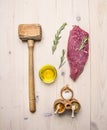 Concept cooking raw beef steak, rosemary, wooden hammer for beating the meat, oil, herbs spices on wooden rustic background to Royalty Free Stock Photo