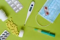 Still life of pharmaceutical items. Mask, thermometer, medications, syringe. Green background