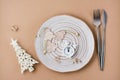 Concept Countdown on Christmas night. Table setting. Alarm clock and Christmas decorations on a plate and cutlery on a beige Royalty Free Stock Photo