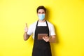 Concept of covid-19, small business and pandemic. Friendly waiter in medical mask and black apron showing thumb up