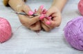 The concept of crocheting products.Crochet hook in women`s hands with a pink manicure among multi-colored skeins, gray background