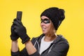 The concept of cybercrime and hacking. Portrait of a woman in a black hat, gloves and mask, who is holding a mobile phone. Yellow