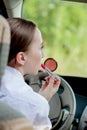 Concept of danger driving. Young woman driver red haired teenage girl painting her lips doing applying make up while driving the