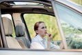 Concept of danger driving. Young woman driver red haired teenage girl painting her lips doing applying make up while driving the