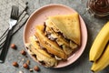 Concept of delicious breakfast with crepes with chocolate paste, banana and nuts on gray background
