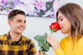 Sensual girl smells a rose her boyfriend gave her. He looks at her with love, pleased that she likes his present.