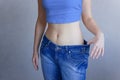 The concept of diet and weight loss. A woman in large jeans on a blue background shows her slender stomach. Liposuction