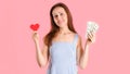 The concept of a difficult choice between money and love. A woman holds money and a red heart symbol in her hands. Studio shot on Royalty Free Stock Photo