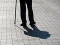 Silhouette of limping man walking with a cane, long shadow on pavement