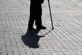 Silhouette of old person walking with a cane, long shadow on pavement