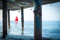 Concept of discovery, hope and travel - a sailboat with a red sail floats by the sea. View from the old pillars of the pier. Royalty Free Stock Photo