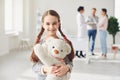 Girl with a toy stands against the background of the doctor and parents standing in the clinic office.