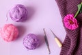 The concept of doing needlework in your free time. Skeins of yarn on a knitted fabric, a lilac flower, knitting tools on a light