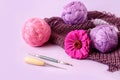 The concept of doing needlework in your free time. Skeins of yarn on a knitted fabric, a lilac flower, knitting tools on a light