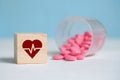 The concept of a daily dose of medication for the heart. Icon on a wooden square next to tablets made of plastic cup