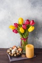 Concept Easter, tulips in a vase and a basket of eggs, a candle on a gray background. Copy space for product or text Royalty Free Stock Photo