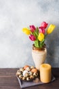 Concept Easter, tulips in a vase and a basket of eggs, a candle on a gray background. Copy space for product or text Royalty Free Stock Photo