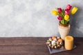 Concept Easter, tulips in a vase and a basket of eggs, a candle on a gray background. Copy space for product or text Royalty Free Stock Photo