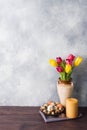 Concept Easter, tulips in a vase and a basket of eggs, a candle on a gray background. Copy space for product or text Royalty Free Stock Photo