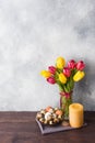 Concept Easter, tulips in a vase and a basket of eggs, a candle on a gray background. Copy space for product or text Royalty Free Stock Photo