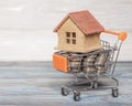 The concept of ECO-houses in the shopping cart full of coins on the background texture of natural wood. Royalty Free Stock Photo