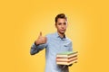 Concept of education, back to school. Young Caucasian teenager in a blue shirt, holding books in hand and showing a thumbs up.