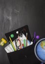 Concept of education, school children and students. Black backpack with stationery and a globe, black background, top view. Free s