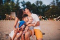 The concept of a family vacation. Young family sitting on a bench in the evening on a sandy beach. Mom and Dad kiss, the older bro Royalty Free Stock Photo