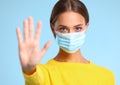 Concept of fighting coronavirus infection. woman in a protective medical mask and yellow sweater shows stop symbol with hand