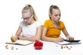 Concept of Finances. Pair of Caucasian Twin Teenage Girls With Notebooks Making Notes. With Stacks of Coins and Moneybox in