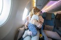 Concept of flight with a child. little cute toddler jumping on her knees with a young beautiful mother in an airplane